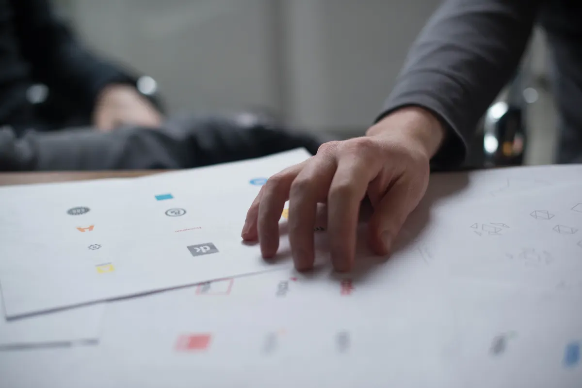 Close-up of a hand reviewing logo design concepts on paper during a client review